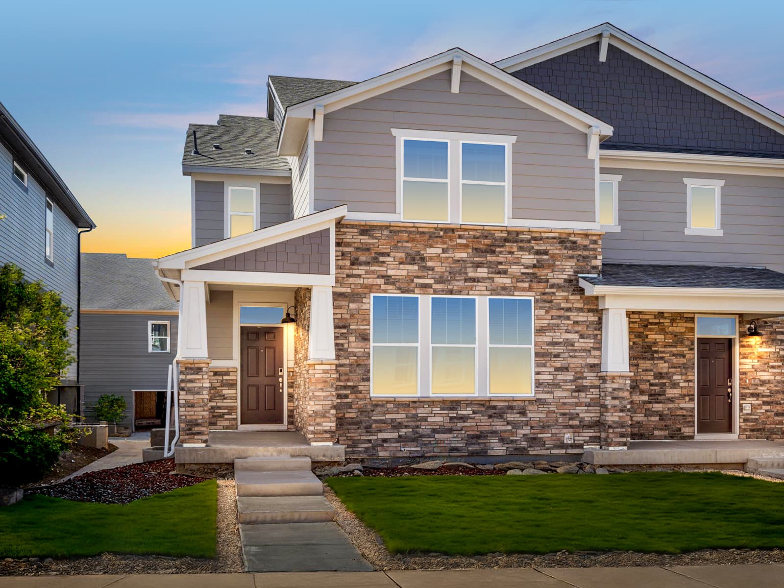 Two-story suburban house with gray siding, stone facade, and white trim in Horizon Uptown Aurora CO. Steps lead to a covered entrance with a brown front door—perfect for those seeking aurora co new home communities.