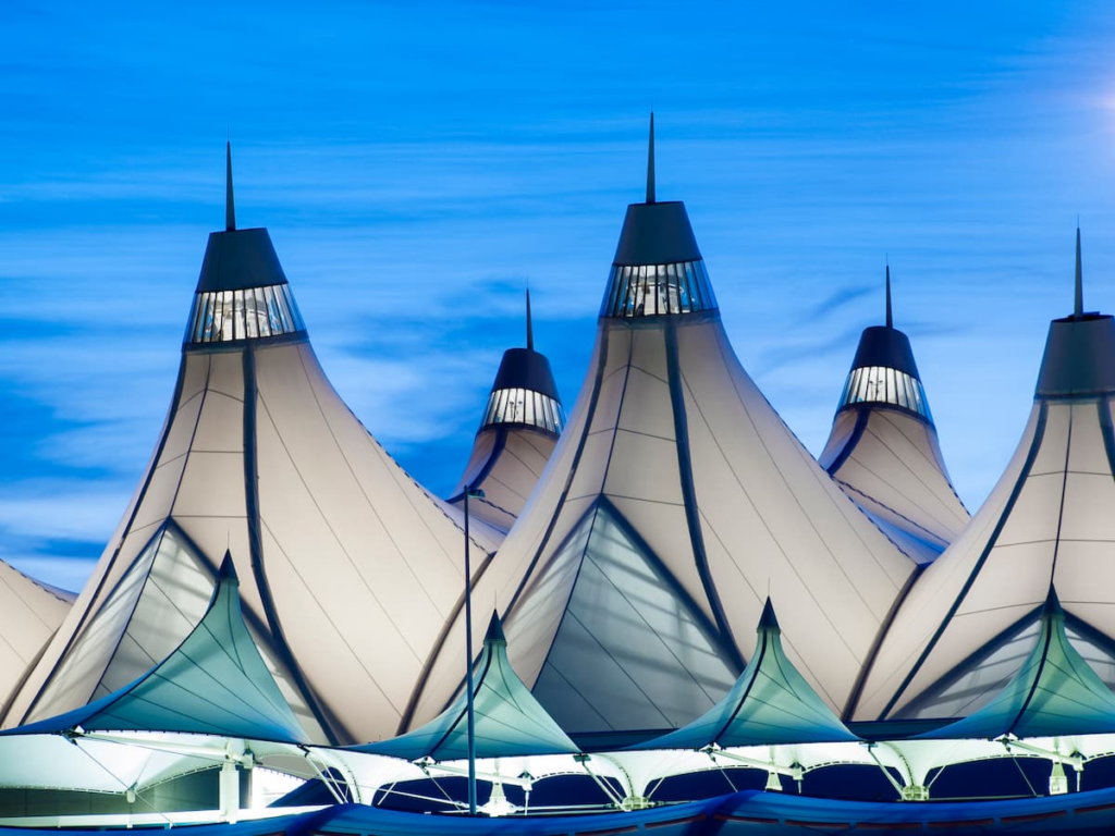 White tensile fabric structures with pointed peaks at Denver International Airport, photographed at dusk against a blue sky, echo the modern design found in Horizon Uptown Aurora CO new home communities.