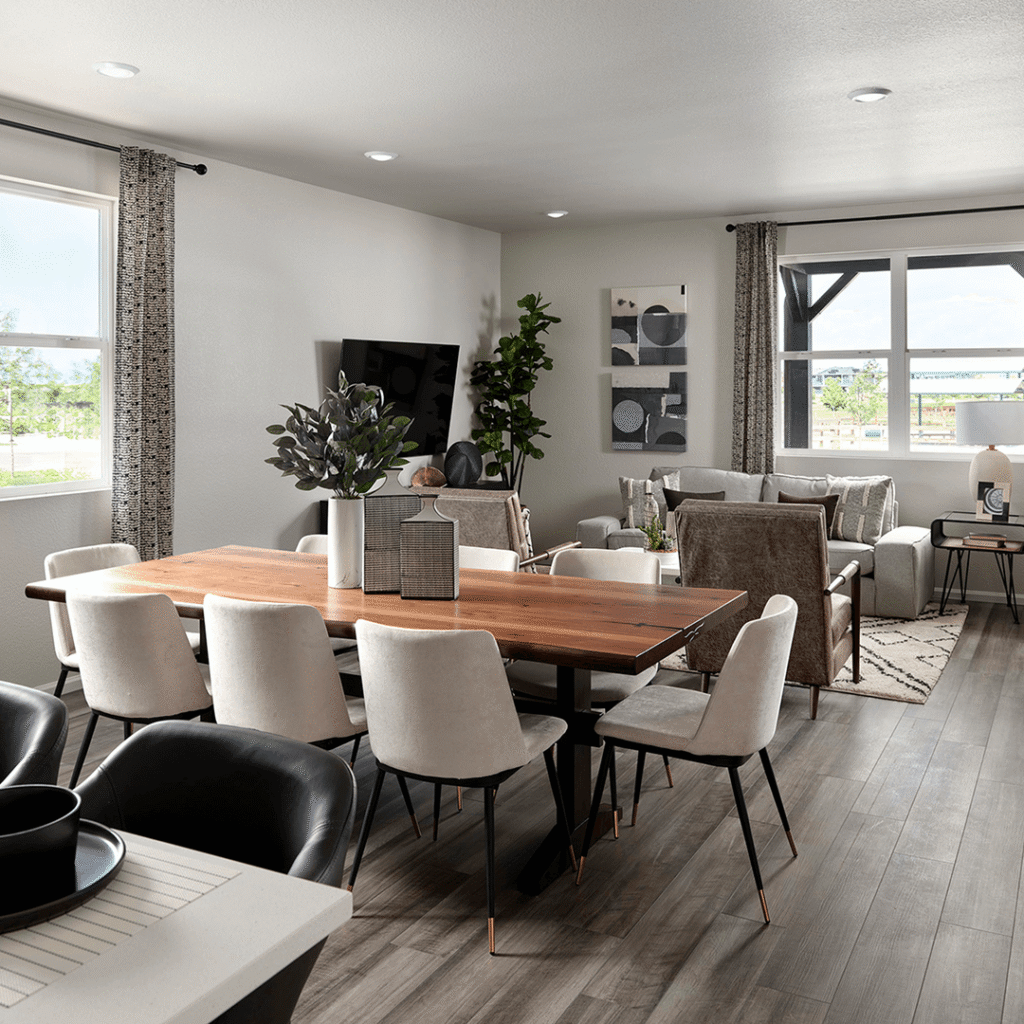 Modern open-concept dining and living room in Horizon Uptown Aurora with light walls, wood flooring, a wooden dining table, white chairs, and large windows letting in natural light—discover new homes in Aurora CO today.