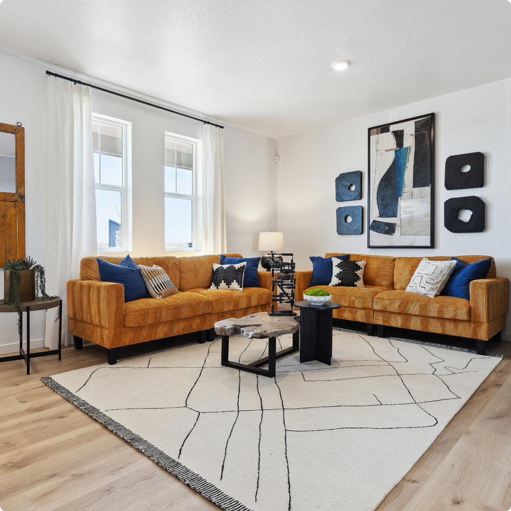 Modern living room in Horizon Uptown Aurora with two orange sofas, blue and white pillows, a geometric rug, abstract wall art, and round nesting coffee tables on light wood flooring—perfect for new homes in Aurora CO.
