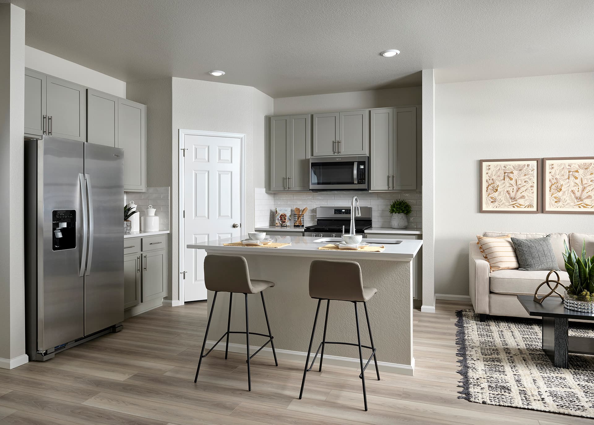 Modern kitchen with gray cabinets, stainless steel appliances, a center island with barstools, and an adjacent living area—this inviting space showcases the style of new homes in Aurora CO at Horizon Uptown Aurora CO.