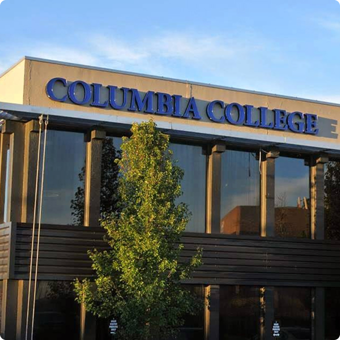 The front exterior of a building with large blue letters spelling "Columbia College" above windows; a tree is in the foreground, near the vibrant community of Horizon Uptown homes for sale in Aurora.